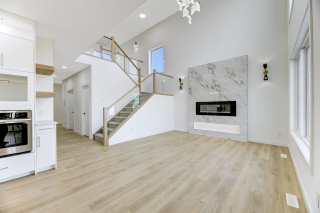 Open-concept living room with tiled fireplace, light wood flooring, and glass-railed staircase in a Vita Homes model in Edmonton and Beaumont
