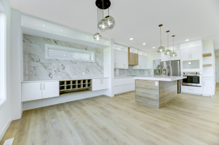 Luxury kitchen in the Aria model by Vita Homes featuring a full marble backsplash wall, built-in wine rack, modern pendant lighting, and sleek open-concept kitchen