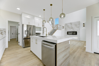 Modern kitchen with island sink, stainless steel appliances, pendant lighting, and open sightlines to the living room in the Aria model by Vita Homes