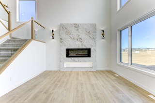 Modern living room with large windows, Tile feature wall, and built-in electric fireplace in the Aria model by Vita Homes