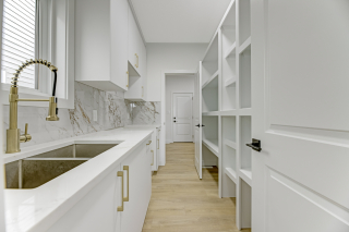 Spicy kitchen with deep sink, white cabinetry, marble backsplash, and adjacent walk-in pantry in the Aria model by Vita Homes