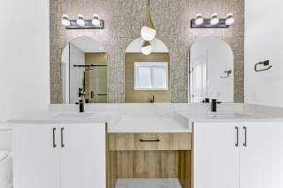 Modern double vanity bathroom with arched mirrors, black fixtures, and statement lighting in a Vita Homes ensuite