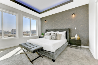 Spacious primary bedroom in the Venetian model with large windows, accent wall, and tray ceiling lighting - Vita Homes Edmonton and Beaumont